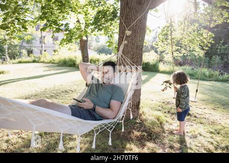 Mann, der in der Hängematte im Garten liegt und Telefon benutzt Stockfoto