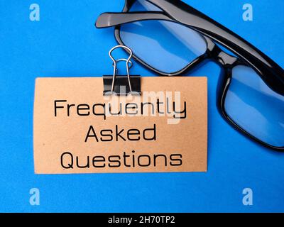 Braune Karte und Brille mit Text geschrieben Häufig gestellte Fragen auf blauem Hintergrund. Stockfoto