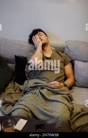 Kranker Mann auf dem Sofa mit Gesicht in den Händen Stockfoto