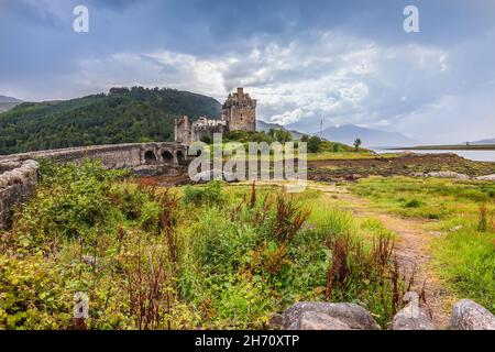 Eilean Donan Castle in Schottland auf einer Insel. Berge und See im Hintergrund der historischen Burg. Steinbrücke für Fußgänger und Gras Stockfoto