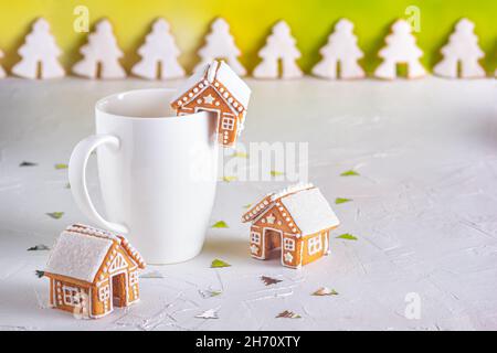 Lebkuchenhütten und eine Tasse Milch auf einer weißen Betonoberfläche mit Funkeln, Nahaufnahme. Weihnachtsfeier Konzept Stockfoto