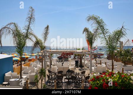 Blick auf eine Strandbar mit Tischen und Stühlen an der Küste von Alassio an einem sonnigen Sommertag, Savona, Ligurien, Italien Stockfoto