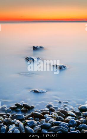 Blick von Arbon über den Bodensee bei Sonnenaufgang, mit Steinen im Vordergrund und mit langsamer Verschlusszeit fotografiert, Schweiz Stockfoto