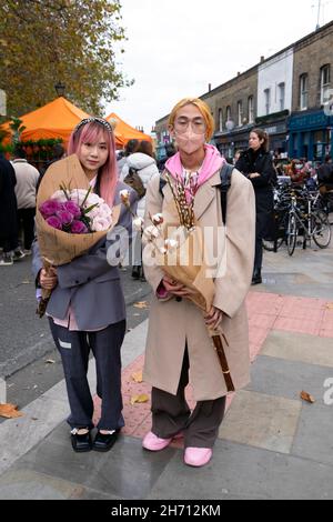 Columbia Road Flower Market Asiatischer Mann trägt covid Gesichtsmaske Gesichtsmasken Frau hält rosa Rosen Blumen in der Straße 2021 East London UK KATHY DEWITT Stockfoto