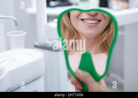 Beschnittene Nahaufnahme einer unkenntlich lächelnden Frau im Handspiegel mit ihren gesunden weißen Zähnen in der Zahnklinik Stockfoto