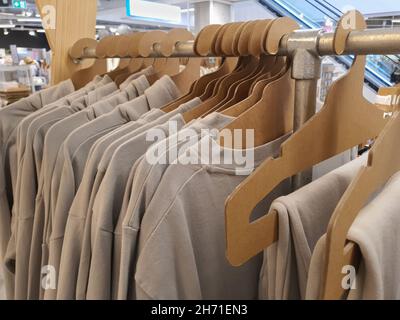 Kleidung in trendigen natürlichen Farben hängt auf umweltfreundlichen Papppapierhaltern auf dem Regal im Bekleidungsgeschäft, Pastelltöne. Selektiver Fokus Stockfoto