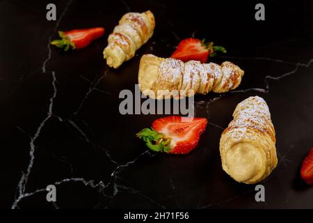 Knusprige süße Brötchen mit Schlagsahne und Erdbeeren auf schwarzem Hintergrund. Stockfoto