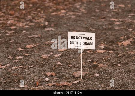 Informationsschild im Park mit der Inschrift in Englisch'do not walk on the Grass'on the background of a Brown soil and dry blättrig in morning hoar Stockfoto