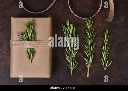 Flaches Stillleben mit einem schlichten braunen Papier eingewickelt Geschenk, Rosmarin Zweige und Sackleinen Band. Stockfoto