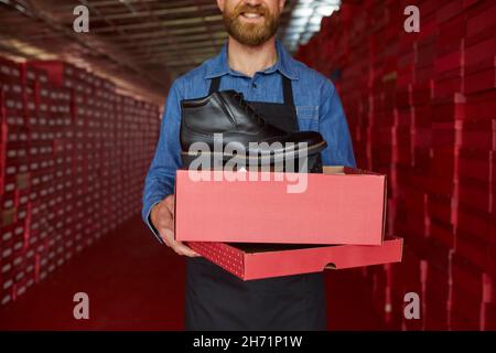 Lagerarbeiter oder Besitzer einer Schuhfabrik, die einen neuen schwarzen Lederstiefel zeigt Stockfoto