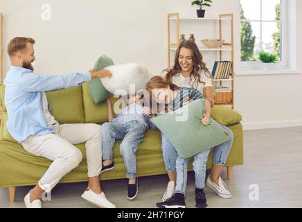 Fröhliche Mutter, Vater und Kinder kämpfen mit Kissen auf der Couch im Wohnzimmer Stockfoto