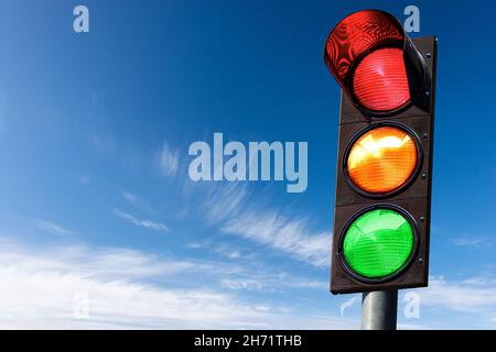 Nahaufnahme einer Ampel auf einem blauen Himmel mit Wolken und Kopierraum, alle drei Lichter an, grün, orange und rot. Italien, Europa. Stockfoto