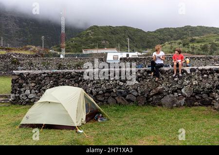 Mutter und Sohn frühstücken auf einer Steinmauer am Zelt auf dem Campingplatz in Faja Grande, Flores, azoren, Portugal Stockfoto