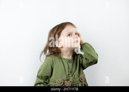 Kleine rothaarige Vorschulmädchen auf weißem Hintergrund sieht nachdenklich aus. Studiofoto des denkenden Kindes Stockfoto