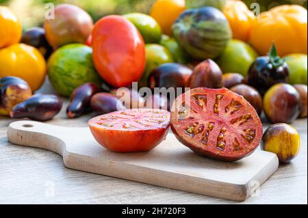 Tisch mit einem Schneidebrett mit geschnittenen Tomaten und verschieden farbigen Tomaten im Hintergrund Stockfoto