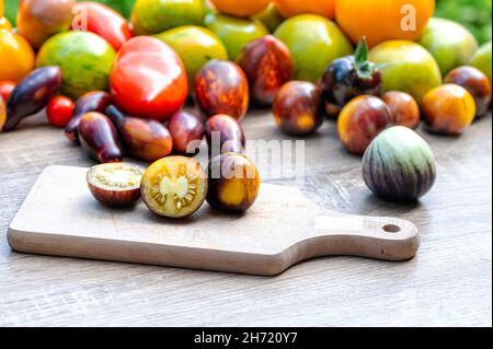 Tisch mit einem Schneidebrett mit geschnittenen Tomaten und verschieden farbigen Tomaten im Hintergrund Stockfoto