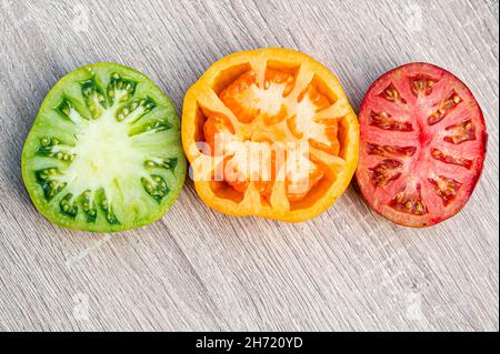 Rote, gelbe und grüne Tomatenhälften auf einem Holztisch, Nahaufnahme von oben, abstrakte Semaphore Stockfoto