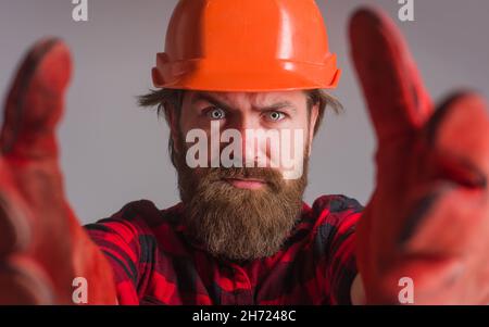 Builder in Helm. Arbeiter in Hardhut und Arbeitshandschuhen. Gebäude, Industrie, Technologie. Bärtige Arbeiter Nahaufnahme. Selektiver Fokus. Stockfoto