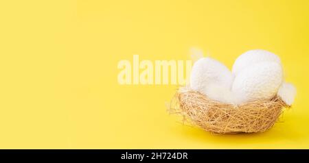 Weiß strukturierte Hühnereier in einem Strohkorb oder Strohnest, Nahaufnahme, auf einem gelben Hintergrund. Osterkarte Gruß, Banner. Speicherplatz kopieren. Stockfoto
