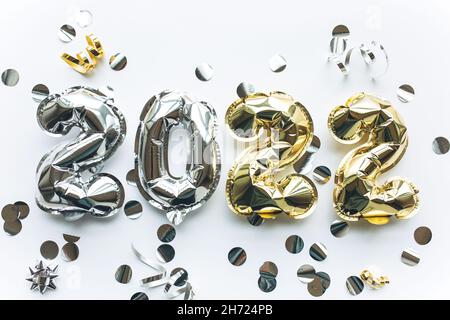 Luftballons aus Gold- und Silberfolie in Form von Zahlen 2022 mit Konfetti auf weißem Hintergrund. Weihnachten, Neujahr und festliches Konzept feiern. Stockfoto