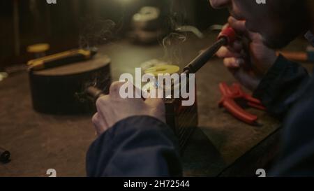 Nahaufnahme eines jungen Technikers, der das Kabel auf eine Batterie auf der Werkbank lötet Stockfoto