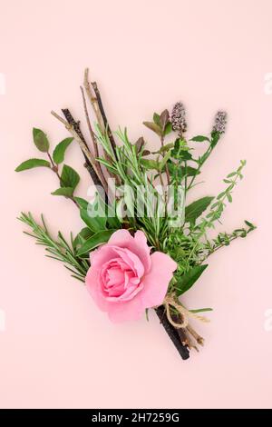 Liebestrank mit Kräutern und Rosenblüten auf rosa Hintergrund gebunden. Hexenbündel enthält Rosmarin, Minze, Lorbeerblätter, Zweige. Romantisches Zauberkonzept. Stockfoto