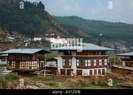Traditionelle bhutanische Bauernhäuser vor dem Paro Rinchen Pung Dzong in Paro, Bhutan. Das Zuri Dzong liegt auf dem Hügel oben. Stockfoto