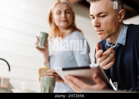 Ehepaar, Frau und Mann, die am Morgen vor der Arbeit frühstücken und an einem Tablet arbeiten Stockfoto