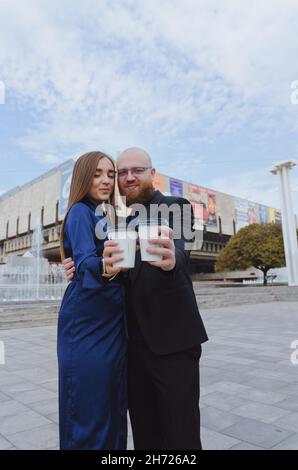 Glückliche Familie, ein Paar, das in der Stadt Kaffee trinkt. Urbane Liebesgeschichte eines stylischen jungen Geschäftsmanns in einem blauen Anzug mit rotem Bart. Und attraktive Frau Stockfoto