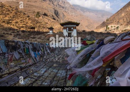 Gebetsfahnen säumen die eiserne Kettenbrücke über den Paro Chhu River in der Nähe des Tamchhog Lhakhang Tempels in Bhutan. Stockfoto