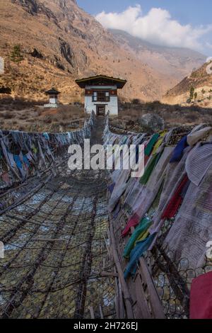 Gebetsfahnen säumen die eiserne Kettenbrücke über den Paro Chhu River in der Nähe des Tamchhog Lhakhang Tempels in Bhutan. Stockfoto