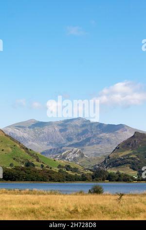 Wunderschöner See Nantlle, Snowdonia, Wales. Vertikale Aufnahme mit Vordergrund von Wasser und Wiese. Dramatischer, robuster Mount Snowdon im Hintergrund. Kopie sp Stockfoto