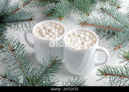 Zwei weiße Becher mit heißer Schokolade mit Marschall und Weihnachtsbaum auf weißem Holztisch. Kakao-Getränk am Morgen mit Neujahrsdekoration, Fichte Stockfoto