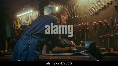 Schmied männliche Person in ehrfürchtigen Werkstatt Hintergrund er ein Stück Eisen oder Stahl in seiner Werkstatt, Weitwinkel-Rückansicht Schleifen Stockfoto