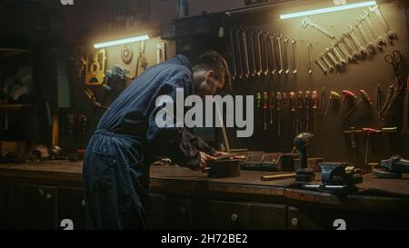 Schmied männliche Person in ehrfürchtigen Werkstatt Hintergrund er ein Stück Eisen oder Stahl in seiner Werkstatt, Weitwinkel-Rückansicht Schleifen Stockfoto