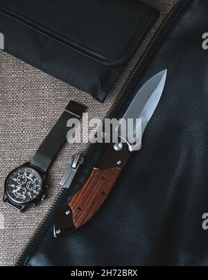 BRASOV, RUMÄNIEN - 31. Mai 2021: Flache Verlegung eines EDC-Klappmessers und einer schwarzen Uhr auf einer Leder- und braunen Textur Stockfoto