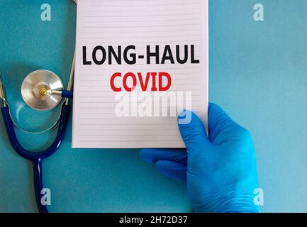COVID-19 Symbol für langstreckige kovide Symptome. Weiße Karte mit den Worten Langstrecke covid. Arzthand, Stethoskop, schöner blauer Hintergrund, Kopierraum. Medi Stockfoto