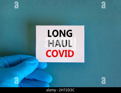 COVID-19 Symbol für langstreckige kovide Symptome. Weiße Karte mit Worten Langstrecke covid. Arzthand, schöner blauer Hintergrund, Kopierraum. Medizinisch, COVID-19 Stockfoto