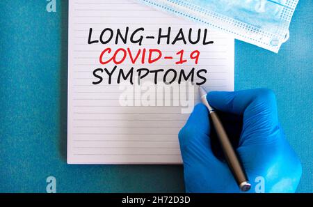 COVID-19 Symbol für langstreckige kovide Symptome. Weiße Karte mit Worten Langstrecke covid-19 Symptome. Arzthand, Stift, blauer Hintergrund, Kopierraum. Medizinisch, C Stockfoto