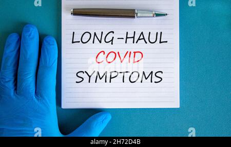 COVID-19 Symbol für langstreckige kovide Symptome. Weiße Karte mit Worten Langstreckensymptome. Arzthand, Stift, blauer Hintergrund, Kopierraum. Medizin, COVI Stockfoto