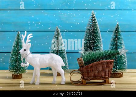 weihnachtsmann Schlitten mit Weihnachtsbaum und weißen Rentieren neben Tannen, während es auf einem Holztisch schneit. Minimales Neujahrskonzept. Stockfoto