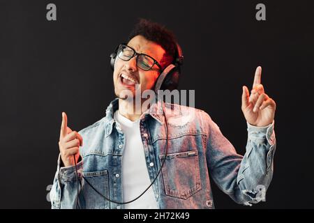 Junger afroamerikanischer Mann, der Kopfhörer trägt und Musik genießen kann Schwarzer Hintergrund Stockfoto