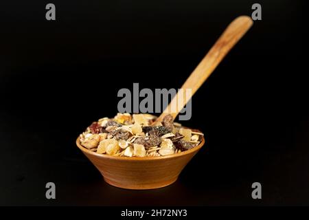 Kleine Holzschale voller Müsli mit getrockneten Früchten, aus der Nähe isoliert auf schwarzem Hintergrund Stockfoto