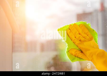 Mit einem gelben Gummihandschuh das Fenster aus der Nähe wischen Stockfoto