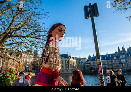 Den Haag, Niederlande. 19th. November 2021. Die kleine Amal sah den sonnigen Tag vor dem Parlamentsgebäude genießen.am letzten Tag ihres Besuchs in den Niederlanden spazierte die riesige Marionette 'Little Amal', ein neunjähriges syrisches Flüchtlingsmädchen und über 11 Meter groß, durch das Stadtzentrum von Den Haag, Wo sich das Repräsentantenhaus befindet, um mit den Menschen auf den Straßen zu interagieren. Dieser Besuch wurde von Amare organisiert, einem neuen kulturellen Zentrum im Rahmen des Open Festivals. Mit ihrem Besuch will Amal in ganz Europa die Aufmerksamkeit auf die Not junger Flüchtlinge lenken, die aus Syrien geflohen sind. Stockfoto