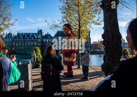 Den Haag, Niederlande. 19th. November 2021. Am letzten Tag ihres Besuchs in den Niederlanden spazierte die riesige Marionette "Little Amal", ein neun Jahre altes syrisches Flüchtlingsmädchen und über 11 Meter groß, durch das Stadtzentrum von Den Haag, wo sich das Repräsentantenhaus befindet, Mit den Menschen auf der Straße zu interagieren. Dieser Besuch wurde von Amare organisiert, einem neuen kulturellen Zentrum im Rahmen des Open Festivals. Mit ihrem Besuch will Amal in ganz Europa die Aufmerksamkeit auf die Not junger Flüchtlinge lenken, die aus Syrien geflohen sind. Während ihres VI Stockfoto