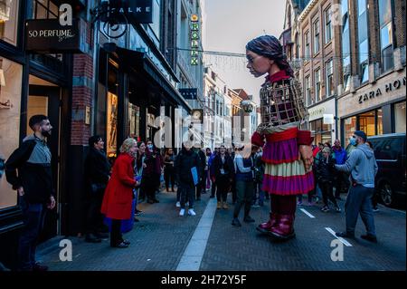 Den Haag, Niederlande. 19th. November 2021. Eine alte Dame sah, wie sie die riesige Marionette Little Amal begrüßte.am letzten Tag ihres Besuchs in den Niederlanden spazierte die riesige Marionette 'Little Amal', ein neun Jahre altes syrisches Flüchtlingsmädchen und über 11 Meter groß, durch das Stadtzentrum von Den Haag, wo sich das Repräsentantenhaus befindet, Mit den Menschen auf der Straße zu interagieren. Dieser Besuch wurde von Amare organisiert, einem neuen kulturellen Zentrum im Rahmen des Open Festivals. Mit ihrem Besuch will Amal in ganz Europa die Aufmerksamkeit auf die Not junger Flüchtlinge lenken, die aus Syrien geflohen sind. Während ihres Besuchs bei der Stockfoto