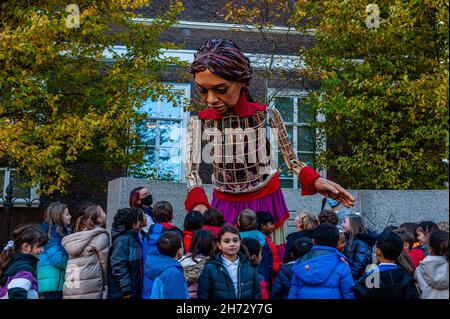 Den Haag, Niederlande. 19th. November 2021. Die kleine Amal, umgeben von einer Gruppe von Kindern einer britischen Schule, wurde am letzten Tag ihres Besuchs in den Niederlanden gesehen.die riesige Marionette 'Little Amal', ein neun Jahre altes Mädchen aus Syrien, war über 11 Meter groß und ging durch das Stadtzentrum von Den Haag. Wo sich das Repräsentantenhaus befindet, um mit den Menschen auf den Straßen zu interagieren. Dieser Besuch wurde von Amare organisiert, einem neuen kulturellen Zentrum im Rahmen des Open Festivals. Mit ihrem Besuch will Amal in ganz Europa die Aufmerksamkeit auf die Not junger Flüchtlinge lenken, die aus Syrien geflohen sind. Während Stockfoto