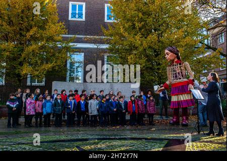 Den Haag, Niederlande. 19th. November 2021. Amal sah die kleine Amal mit einem schönen Lied von Schülern der British School begrüßen.am letzten Tag ihres Besuchs in den Niederlanden spazierte die riesige Puppe 'Little Amal', ein neunjähriges syrisches Flüchtlingsmädchen und über 11 Meter groß, durch das Stadtzentrum von Den Haag. Wo sich das Repräsentantenhaus befindet, um mit den Menschen auf den Straßen zu interagieren. Dieser Besuch wurde von Amare organisiert, einem neuen kulturellen Zentrum im Rahmen des Open Festivals. Mit ihrem Besuch will Amal in ganz Europa die Aufmerksamkeit auf die Notlage junger Flüchtlinge lenken, die aus dem Ausland geflohen sind Stockfoto