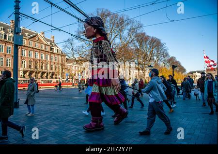 Den Haag, Niederlande. 19th. November 2021. Die kleine Amal sah, wie sie auf den Straßen von neugierigen Menschen folgte.am letzten Tag ihres Besuchs in den Niederlanden spazierte die riesige Marionette "Little Amal", ein neunjähriges syrisches Flüchtlingsmädchen und über 11 Meter groß, durch das Stadtzentrum von Den Haag, wo sich das Repräsentantenhaus befindet, Mit den Menschen auf der Straße zu interagieren. Dieser Besuch wurde von Amare organisiert, einem neuen kulturellen Zentrum im Rahmen des Open Festivals. Mit ihrem Besuch will Amal in ganz Europa die Aufmerksamkeit auf die Not junger Flüchtlinge lenken, die aus Syrien geflohen sind. Während sie Stockfoto